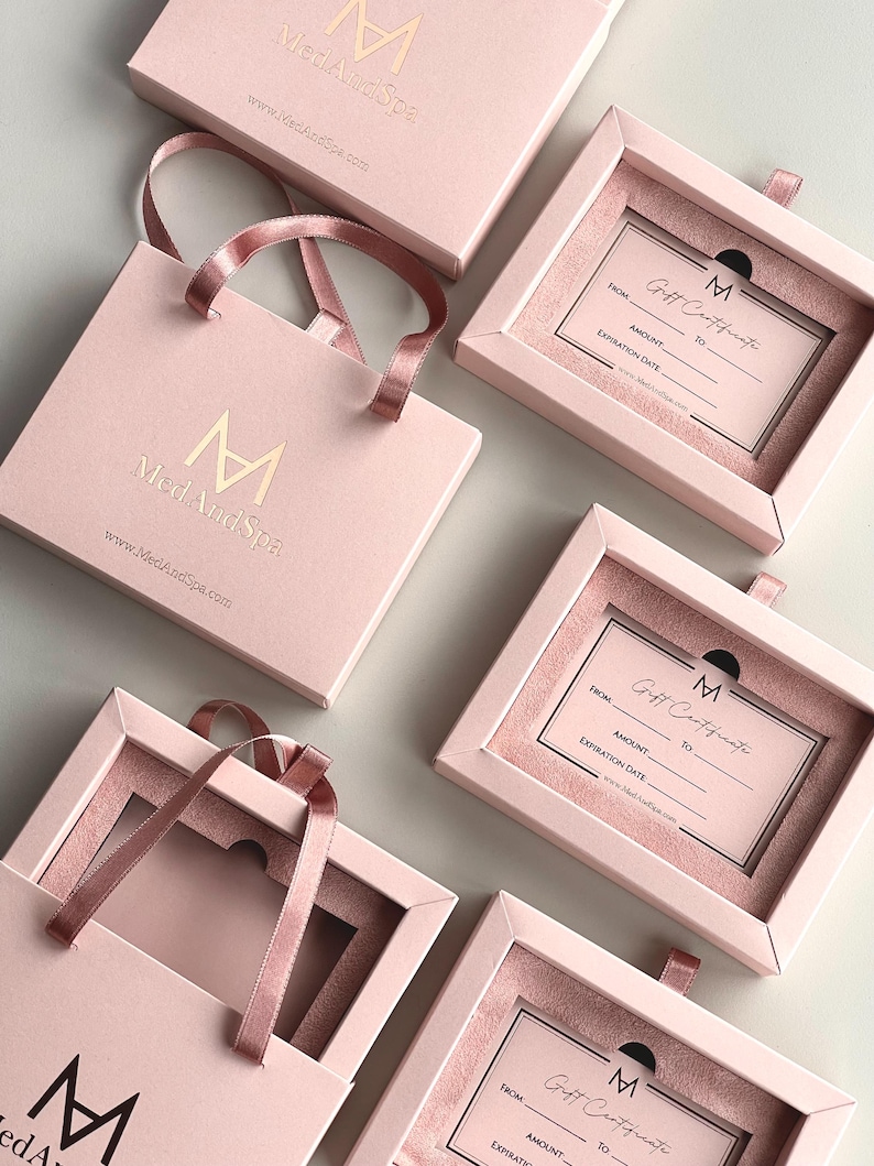 May include: Pink gift boxes and bags with the "MedAndSpa" logo and website address. The boxes contain gift certificates with fill-in fields for "From," "To," "Amount," and "Expiration Date."
