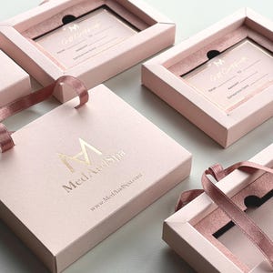 May include: Several pink gift boxes with a ribbon and a gift certificate inside. The gift certificates have gold lettering. The boxes have the logo "Med And Spa" and the website address printed on them.