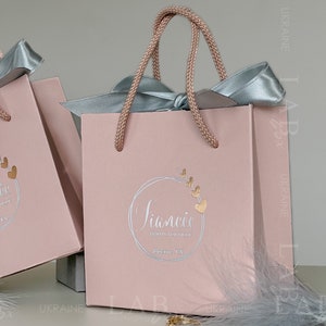 May include: A pink gift bag with a light blue ribbon and a gold logo that says "Siancie Bridal Boutique Bourne, TX".