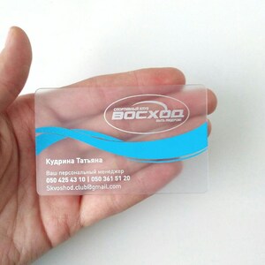 Op de afbeelding: Een transparante plastic visitekaartje met witte tekst en een blauw logo. De tekst luidt "Спортивный клуб Восход быть лидером?" en "Кудрина Татьяна Ваш персональный менеджер 050 425 43 10 | 050 361 51 20 Skvoshod.club@gmail.com".