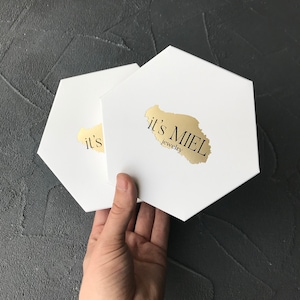 May include: Two white hexagonal boxes with the text "it's MIEL jewelry" on the top box.