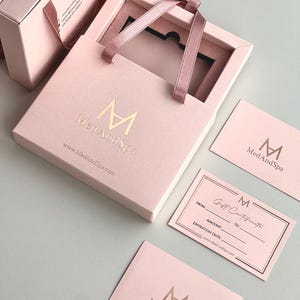 May include: Pink gift boxes and cards with gold foil lettering. The boxes have ribbon handles and the text "MedAndSpa" and website address. One card is a gift certificate with fields for recipient and amount.