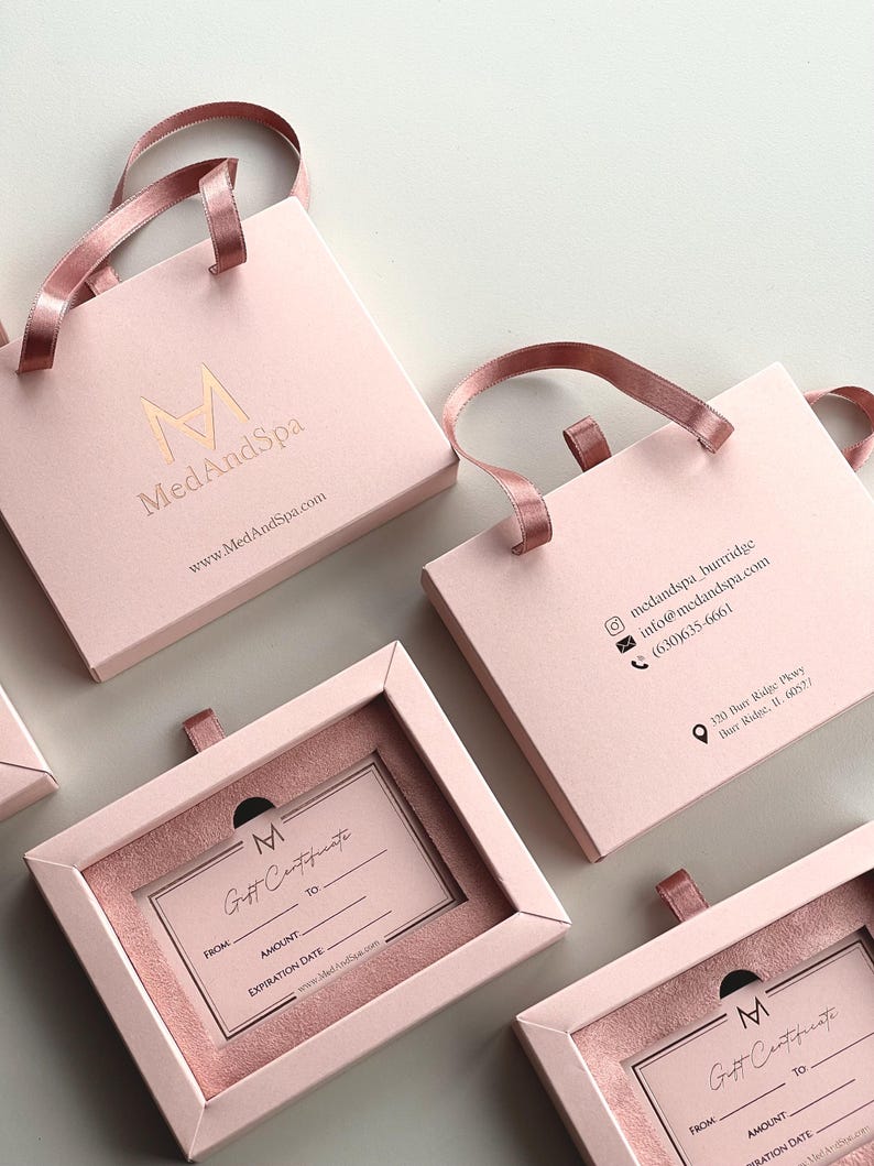 May include: Pink gift boxes with ribbon handles and the "MedAndSpa" logo in gold. Some boxes are open, revealing gift certificates. The gift certificates have space for "From," "Amount," and "Expiration Date."