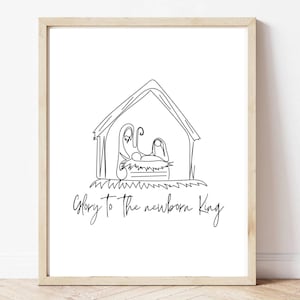 May include: A framed print featuring a minimalist line drawing of a nativity scene. The artwork depicts a stable with figures and the text "Glory to the newborn King" in a handwritten style. The frame is a light wood color.