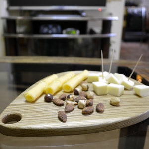 May include: A wooden serving board shaped like a leaf with a handle. The board is filled with cheese cubes, breadsticks, and almonds.