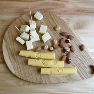 May include: A wooden cutting board with a variety of cheese and nuts. The cheese is cut into cubes and sticks, and the nuts are almonds and hazelnuts.
