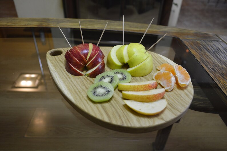 May include: A wooden serving board with a variety of fruit slices, including red apple, green apple, kiwi, and orange. The fruit is arranged in a circular pattern on the board.