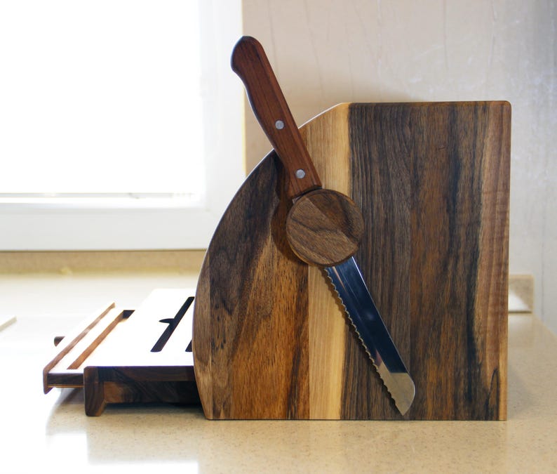 Puede incluir: Una caja de pan de madera con un cuchillo para pan incorporado. La caja est&aacute; hecha de madera oscura con un borde de madera clara. El cuchillo est&aacute; hecho de acero inoxidable y tiene un mango de madera.