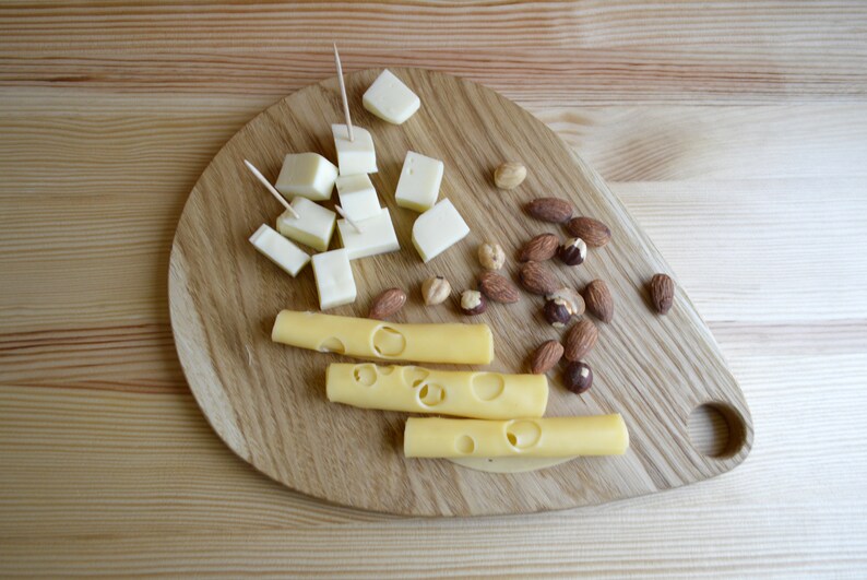May include: A wooden cutting board with a variety of cheese and nuts. The cheese is cut into cubes and sticks, and the nuts are almonds and hazelnuts.