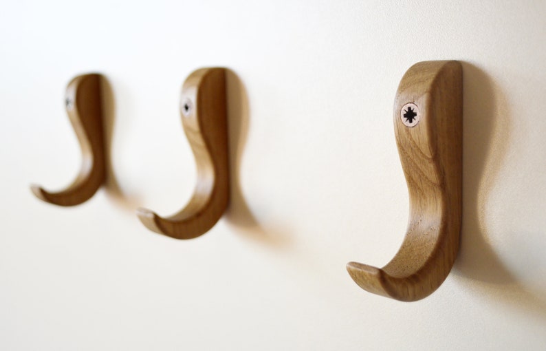 May include: Three wooden hooks mounted on a white wall. The hooks are shaped like a curved 'S' and have a natural wood finish.