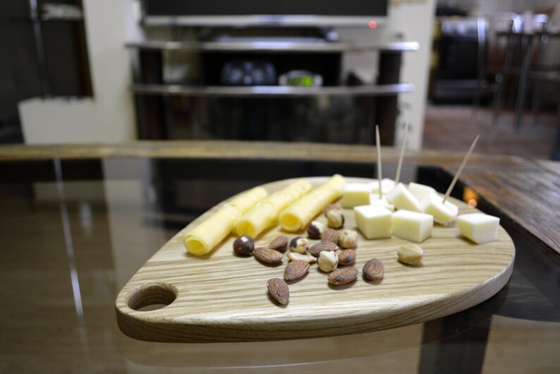 May include: A wooden serving board shaped like a leaf with a handle. The board is filled with cheese cubes, breadsticks, and almonds.