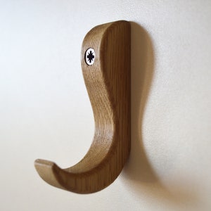 May include: A wooden wall hook with a curved design. The hook is made of light brown wood and has a screw in the top.