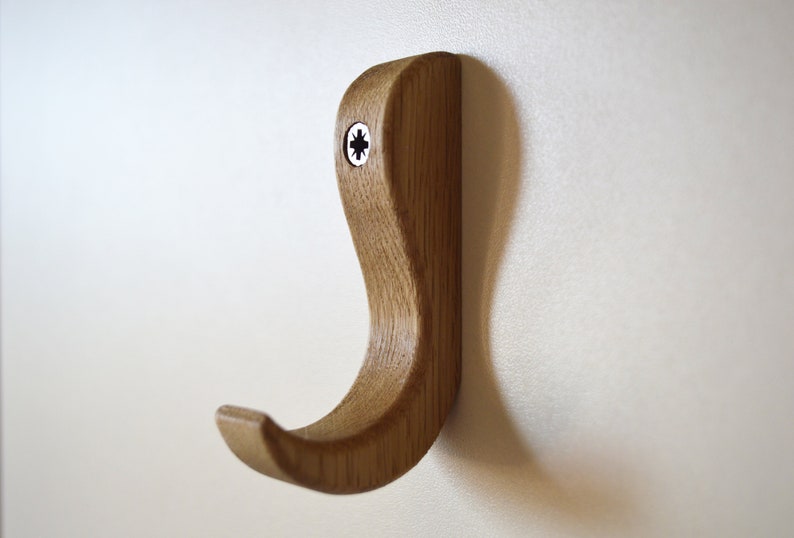 May include: A wooden wall hook with a curved design. The hook is made of light brown wood and has a screw in the top.