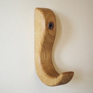 May include: A wooden hook with a curved design, finished in a natural wood tone. The hook is mounted to a wall with a screw.