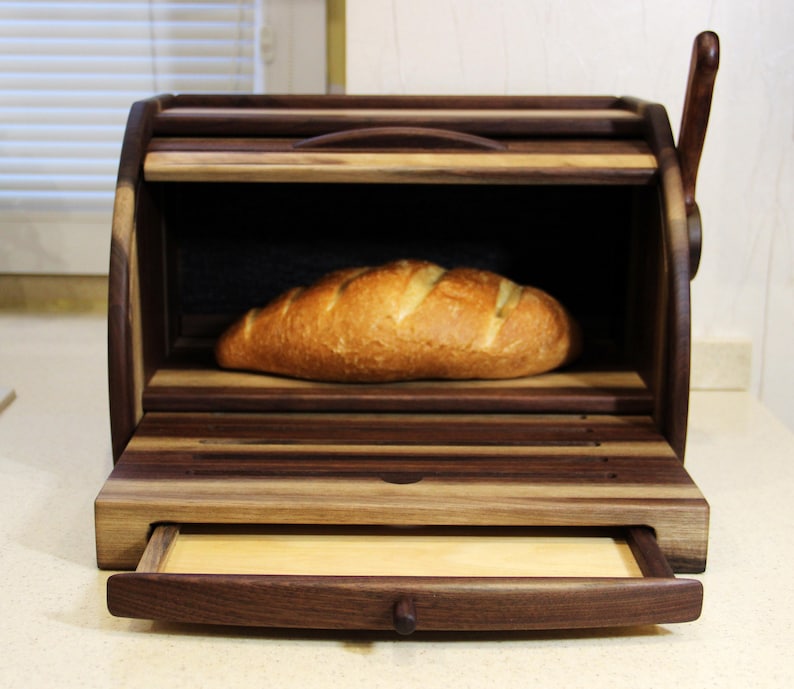 Puede incluir: Una caja de pan de madera con un caj&oacute;n extra&iacute;ble y una hogaza de pan dentro. La caja de pan est&aacute; hecha de madera oscura con un acabado de madera natural.