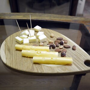 May include: A wooden serving board with a handle, featuring a selection of cheese cubes and cheese sticks, along with almonds and hazelnuts.