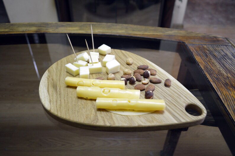 May include: A wooden serving board with a handle, featuring a selection of cheese cubes and cheese sticks, along with almonds and hazelnuts.