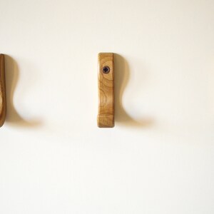 May include: Three wooden wall hooks with a curved design. The hooks are light brown and have a natural wood finish.