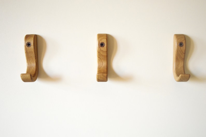 May include: Three wooden wall hooks with a curved design. The hooks are light brown and have a natural wood finish.