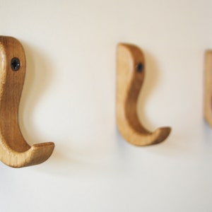 Könnte beinhalten: Drei Holzhaken an einer weißen Wand montiert. Die Haken sind hellbraun und haben ein einfaches, geschwungenes Design.