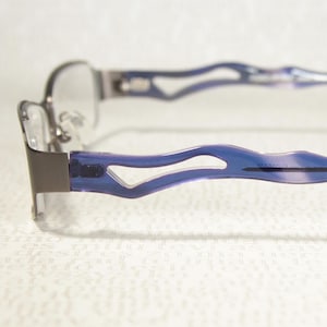 May include: Eyeglasses with a silver metal frame and blue temples. The temples have a unique wave-like design. The lenses are clear. The glasses are designed for vision correction.