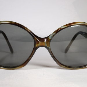 K&ouml;nnte beinhalten: &Uuml;bergro&szlig;e Sonnenbrille mit braunem und hellbraunem Schildpattrahmen und dunkelgrauen Gl&auml;sern. Die Sonnenbrille hat ein abgerundetes, schmetterlingsf&ouml;rmiges Design. Ein Vintage-Accessoire.