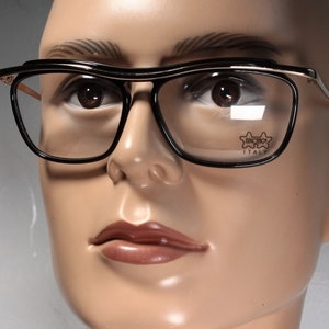 May include: Black framed glasses with gold accents and a clear lens. The glasses have the text "BENCIO" and "ITALY" printed on the lens.