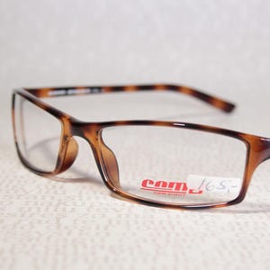 May include: Rectangular spectacles with a tortoiseshell pattern on the frames and arms. The lenses are clear, and the glasses have a small logo on the arm. A price tag is attached to the frame.