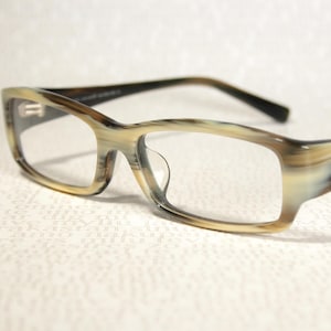 May include: Eyeglasses with a rectangular frame. The frame has a marbled pattern in shades of tan, brown, and cream. The temples are dark brown. The lenses are clear. The glasses are set against a white background.