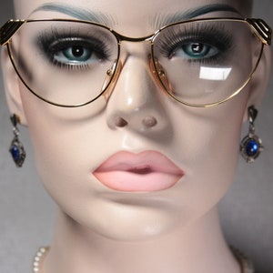 Op de afbeelding: Gouden cat-eye bril met heldere glazen. De bril heeft een delicaat ontwerp met een dun metalen frame.