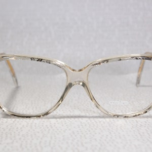 Könnte beinhalten: Transparente Plastikbrille mit einem schwarzen Muster auf dem Rahmen. Der Markenname "carlo" ist am rechten Bügel sichtbar.
