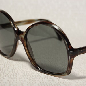May include: Tortoise shell sunglasses with round, dark gray lenses.