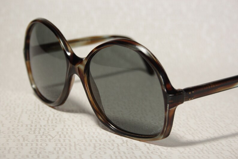May include: Tortoise shell sunglasses with round, dark gray lenses.