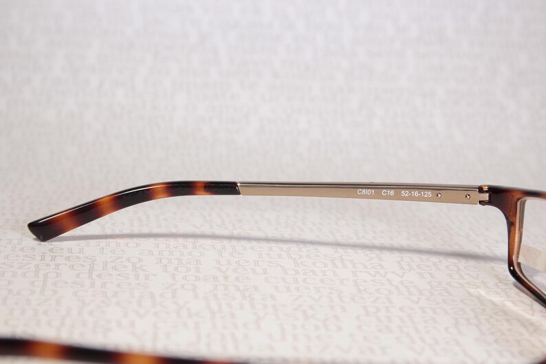 May include: Close-up of eyeglasses with a brown tortoiseshell pattern on the temples and frame. The metal arm is a light gold colour. The text "C801 C16 52-16-125" is printed on the arm.