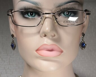 May include: A pair of silver-framed glasses with a rectangular lens shape. The glasses have the text "CHANTAL occhiali" on the right lens.