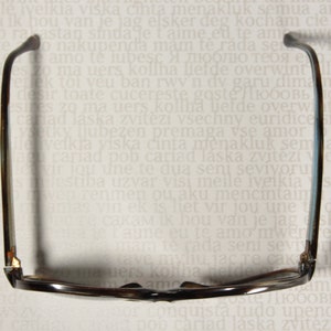 May include: A pair of brown and black eyeglasses with a dark brown frame and lenses. The glasses are lying on a white surface with text.