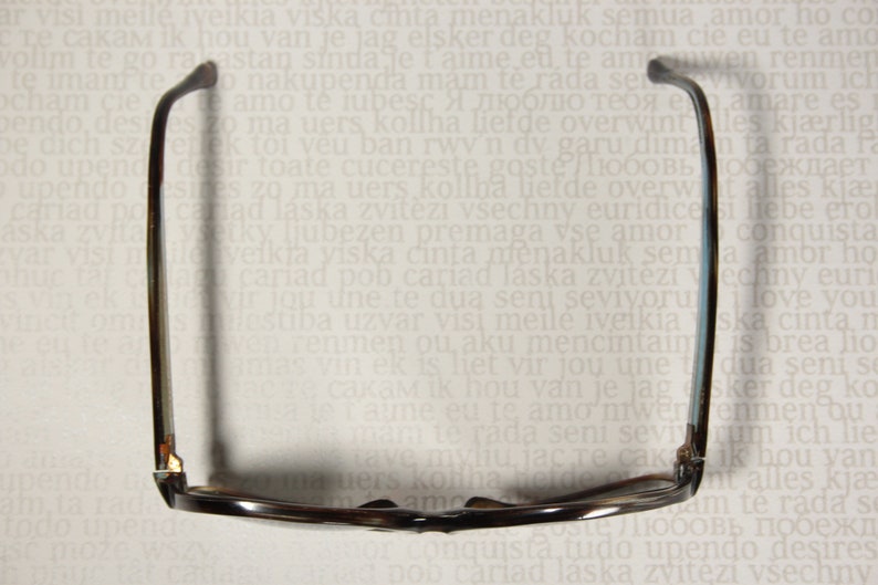 May include: A pair of brown and black eyeglasses with a dark brown frame and lenses. The glasses are lying on a white surface with text.
