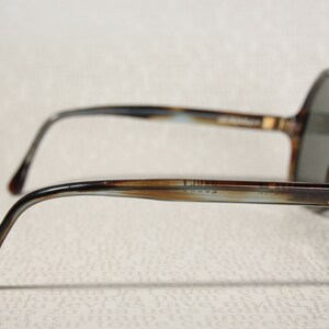 May include: Brown and blue tortoiseshell framed sunglasses with round lenses. The sunglasses have a metal bar connecting the lenses and the arms. The arms are brown and blue tortoiseshell with a gold accent.
