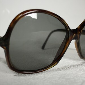 May include: A pair of brown tortoise shell sunglasses with large, round lenses. The lenses are dark gray and the frames are made of plastic.