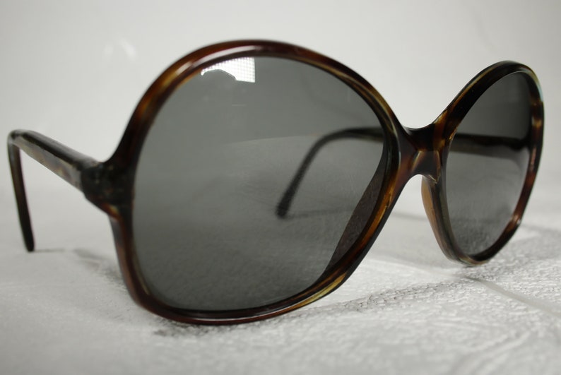 May include: A pair of brown tortoise shell sunglasses with large, round lenses. The lenses are dark gray and the frames are made of plastic.