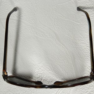 May include: A pair of brown tortoise shell sunglasses with dark lenses. The sunglasses are folded in half and the arms are bent back.