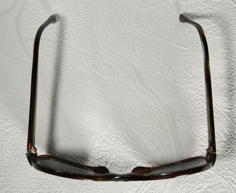 May include: A pair of brown tortoise shell sunglasses with dark lenses. The sunglasses are folded in half and the arms are bent back.