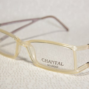 Peut inclure: Une paire de lunettes rectangulaires transparentes avec une monture marron. Le nom de la marque "CHANTAL occhiali" est imprimé sur la lentille droite.