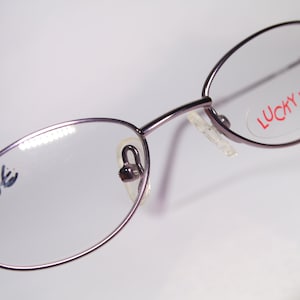 May include: A pair of oval-shaped spectacles with a silver frame and clear lenses. The glasses have a sticker on the right lens that says "LUCKY LOOK" in red letters. The left lens has the number "1166" written on it.
