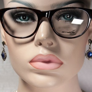 May include: A close-up of a mannequin wearing tortoiseshell eyeglasses with a brown frame and clear lenses. The eyeglasses have the text "arnette optical" printed on the right lens.