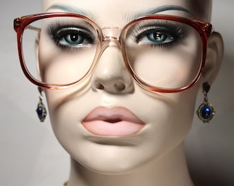 May include: A pair of large, oversized, clear, plastic eyeglasses with a reddish-brown frame. The eyeglasses are on a mannequin's face.