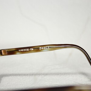 May include: Close-up of the brown tortoiseshell frame of a pair of sunglasses. The frame has the text "GREECE-TH 280C.D" printed on it.