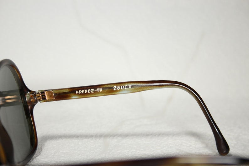 May include: Close-up of the brown tortoiseshell frame of a pair of sunglasses. The frame has the text "GREECE-TH 280C.D" printed on it.