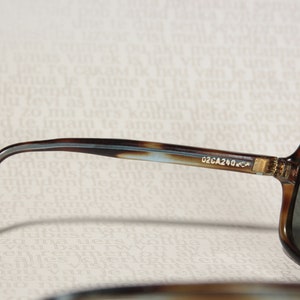 May include: Brown and blue tortoise shell sunglasses with dark gray lenses. The sunglasses have a metal hinge and the text "02CA240-C4" is printed on the side.
