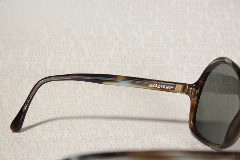 May include: Brown and blue tortoise shell sunglasses with dark gray lenses. The sunglasses have a metal hinge and the text "02CA240-C4" is printed on the side.